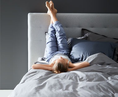 Γυναίκα ξαπλωμένη σε κρεβάτι με τα πόδια στο προσκέφαλο