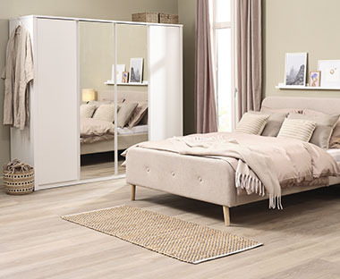 Τετράφυλλη ντουλάπα σε λευκό χρώμα με συρόμενες πόρτες και καθρέφτη σε υπνοδωμάτιο και κρεβάτι διπλό σε μπεζ χρώμα