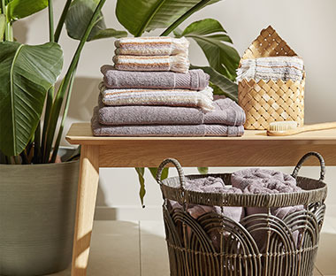 Βαμβακερές πετσέτες μπάνιου, κρεμαστό ψάθινο καλάθι & βούρτσα μπάνιου πάνω σε πάγκο και καλάθι με πετσέτες μπάνιου
