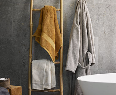 Πετσέτες μπάνιου σε διακοσμητική σκάλα και μπουρνούζι δίπλα από μπανιέρα