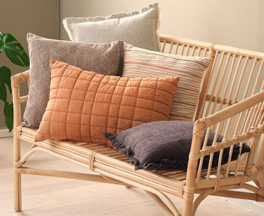 Διακοσμητικά μαξιλάρια σε διάφορα χρώματα και υφές σε καναπέ από ρατάν