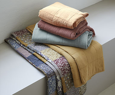 Καλύμματα κρεβατιού σε διάφορα χρώματα και ένα με patchwork