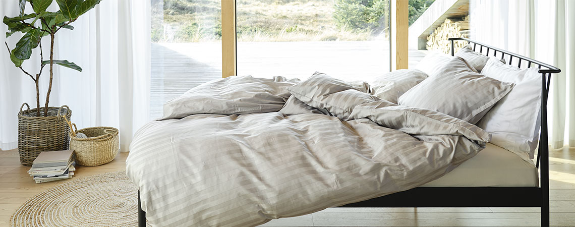Υπνοδωμάτιο με μαύρο μεταλλικό κρεβάτι, πάπλωμα και μαξιλάρια και ριγέ παπλωματοθήκες σε απαλό γκρι και λευκό χρώμα