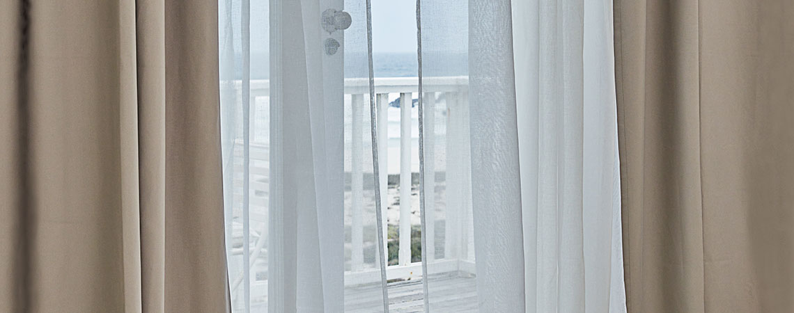 Θέα σε μπαλκόνι από ανοιχτή μπαλκονόπορτα με κουρτίνες που κυματίζουν