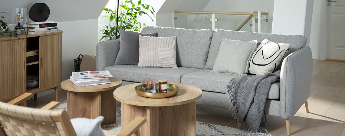 Καθιστικό με γκρι καναπέ με διακοσμητικά μαξιλάρια καναπέ, τραπεζάκια σαλονιού και πολυθρόνες σε σοφίτα