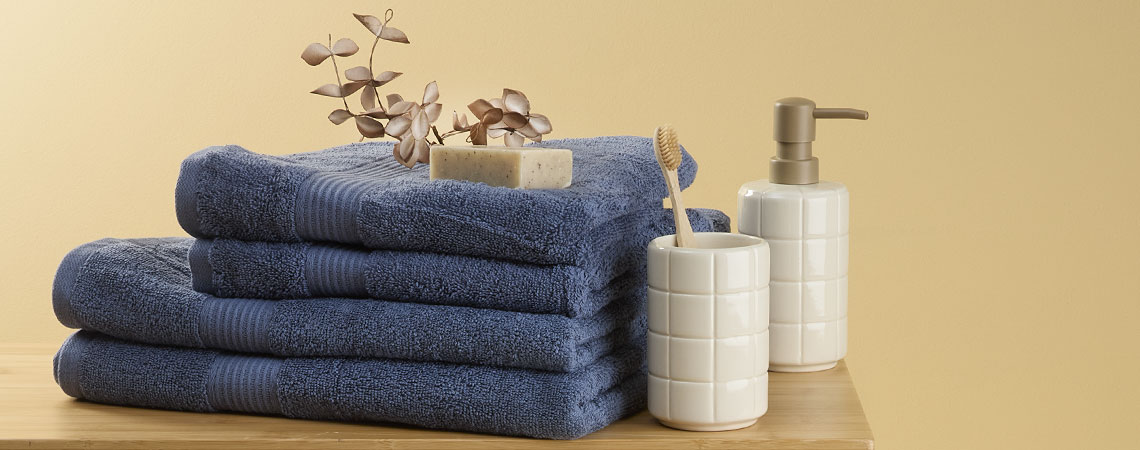 Mπλε πετσέτες μπάνιου σε στοίβα σε έναν πάγκο με μια θήκη οδοντόβουρτσας και ένα δοχείο υγρού σαπουνιού