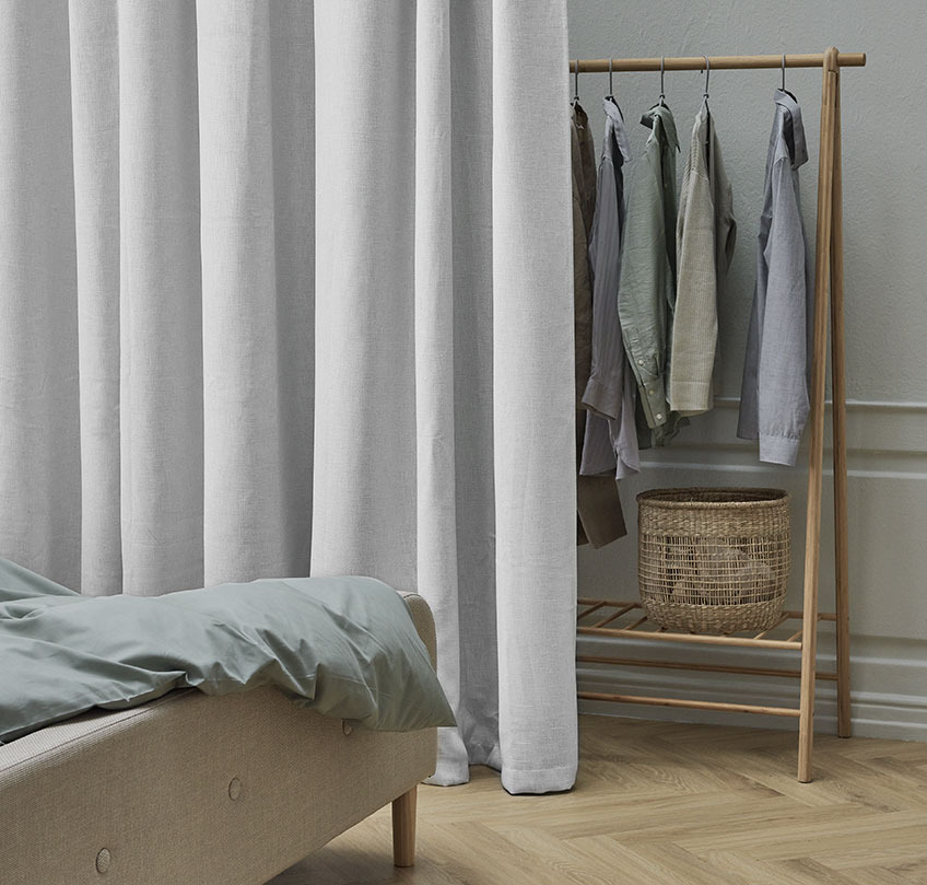 Μπεζ κουρτίνα μπροστά από ράγα ρούχων ως διαχωριστικό ανάμεσα στον χώρο ύπνου και της αποθήκευσης