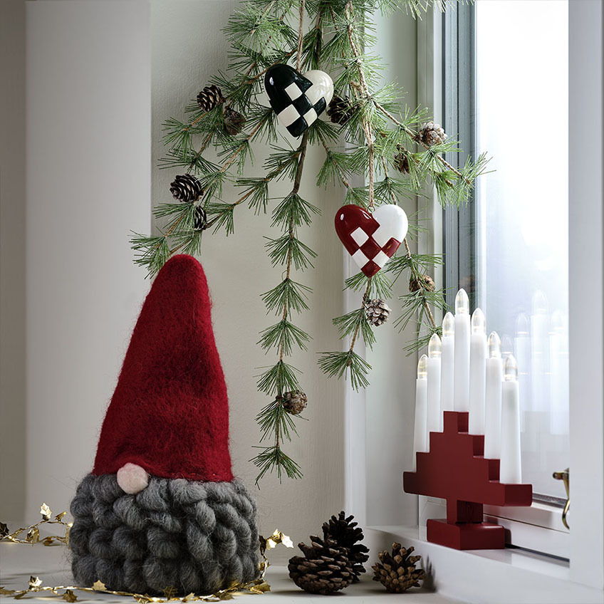 Διακοσμητικός καλικάντζαρος Χριστουγέννων με κόκκινο καπέλο και γκρι μούσια, αψίδα κεριών και χριστουγεννιάτικες διακοσμήσεις