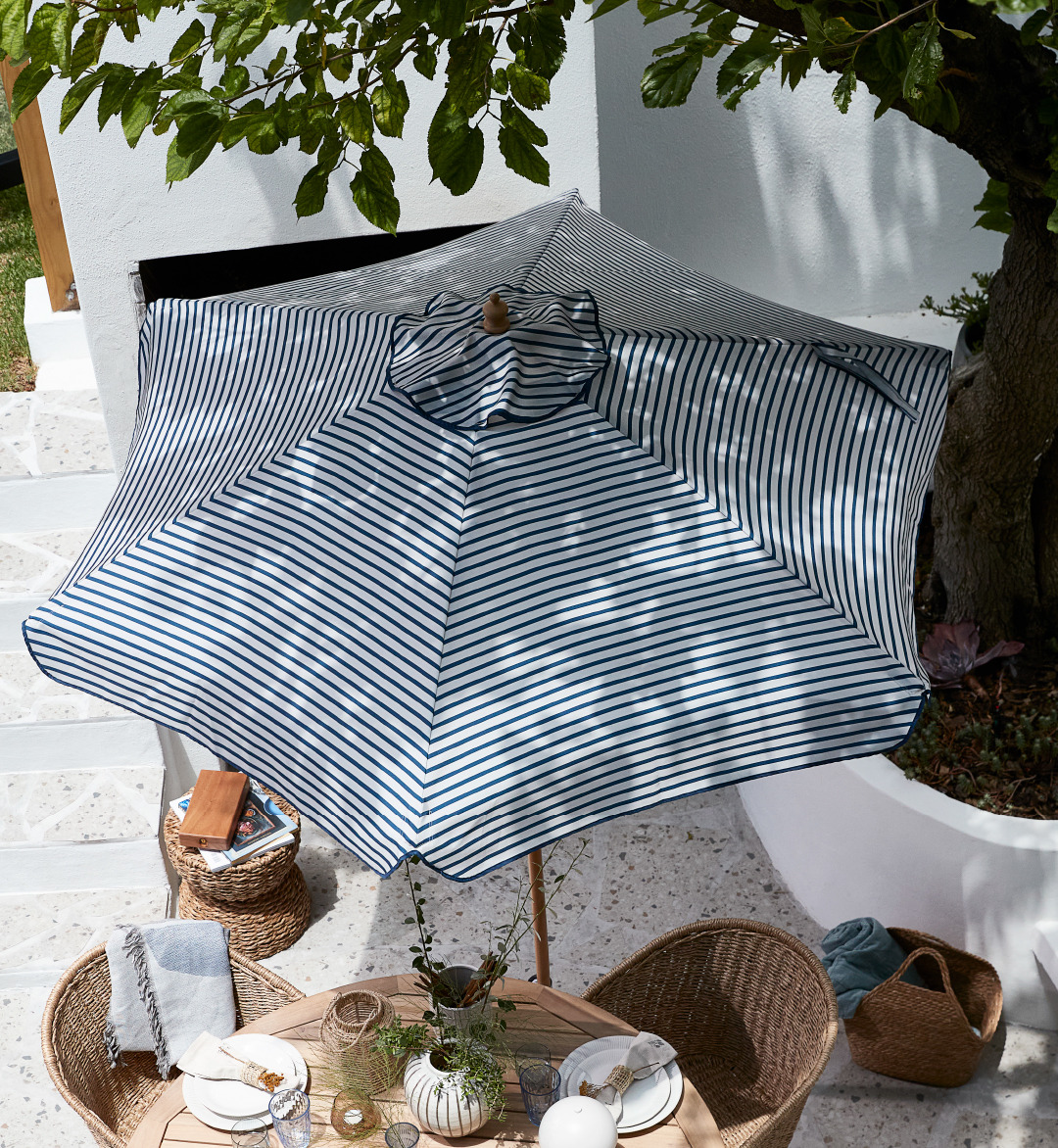 Ριγέ ομπρέλα ήλιου πάνω από σετ τραπεζαρίας κήπου σε αίθριο
