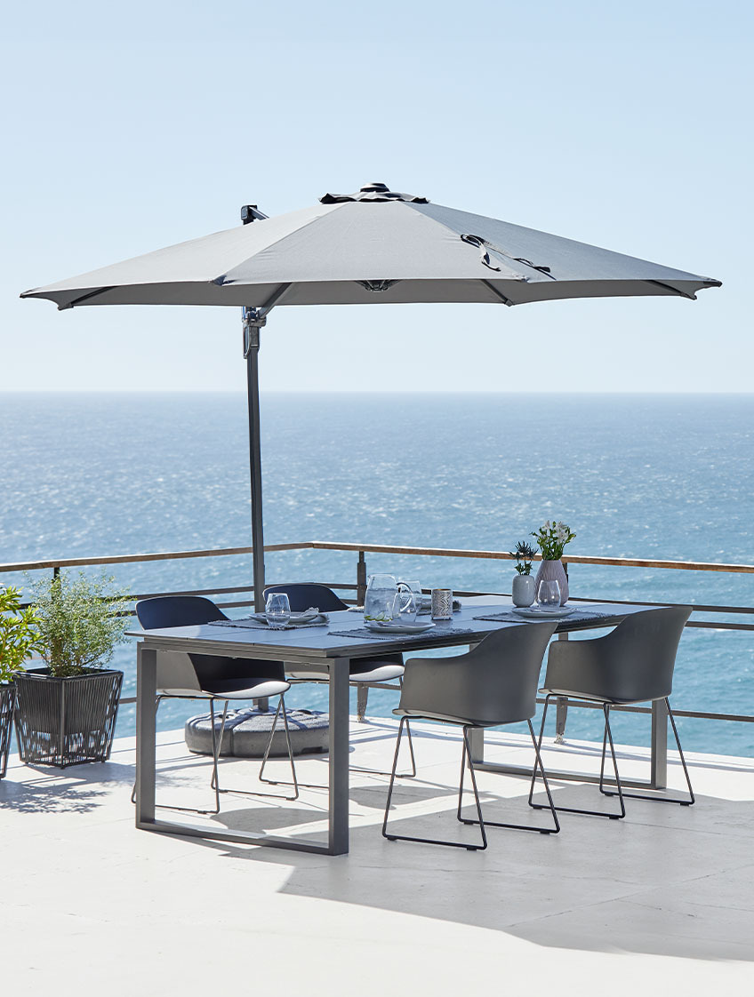 Μεγάλη κρεμαστή ομπρέλα ήλιου σε βεράντα με τραπέζι κήπου και καρέκλες κήπου με θέα τη θάλασσα
