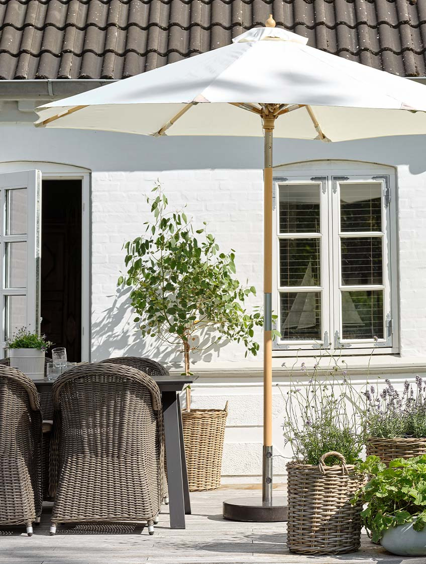 Κλασική ομπρέλα κήπου σε υπόλευκο χρώμα σε αίθριο με τραπέζι κήπου και καρέκλες κήπου