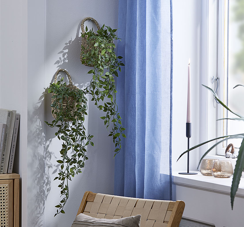 Δύο πλεκτά καλάθια με τεχνητά φυτά που κρέμονται στον τοίχο σαλονιού