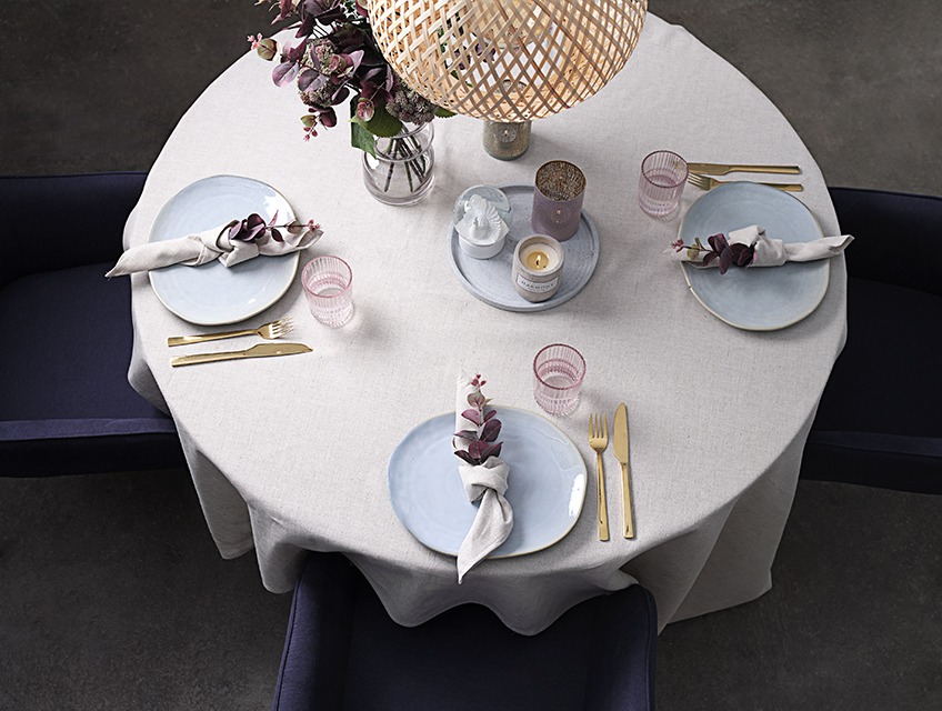 Τραπέζι με σύνθεση από πιάτα, ποτήρια, μαχαιροπίρουνα, βάζο, χαρτοπετσέτες και κεριά πάνω σε τραπεζομάντηλο