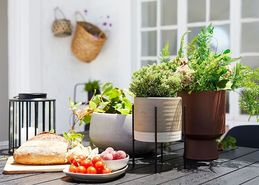 Κεραμικά κασπώ, φανάρι κήπου και δίσκος με ψωμί και φρούτα πάνω σε τραπέζι κήπου