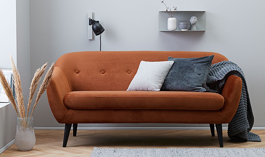 Καθιστικό με πορτοκαλί καναπέ διακοσμημένο με μαξιλαράκια και ριχτάρι
