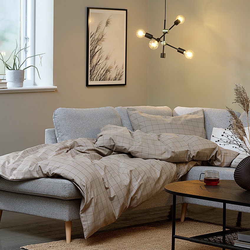 Καθιστικό με ατμόσφαιρα “hygge” με μεγάλο γωνιακό καναπέ, πάπλωμα και κρεμαστό φωτιστικό οροφής