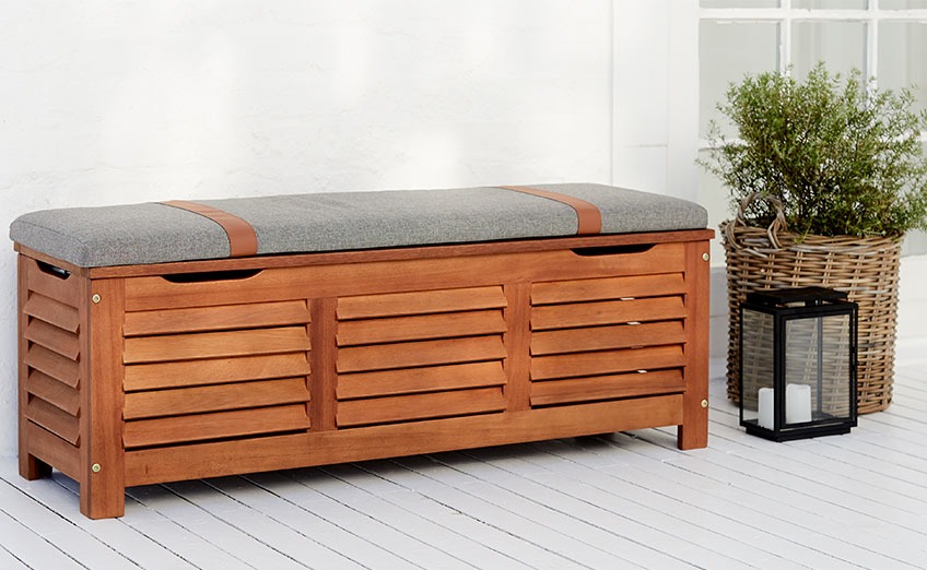 Wooden outdoor storage bench on a patio with planter and lantern