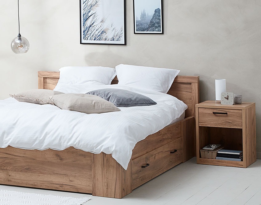 Ένα υπνοδωμάτιο με κρεβάτι που διαθέτει συρτάρια αποθήκευσης και δίπλα του κομοδίνο της ίδιας σειράς επίπλων