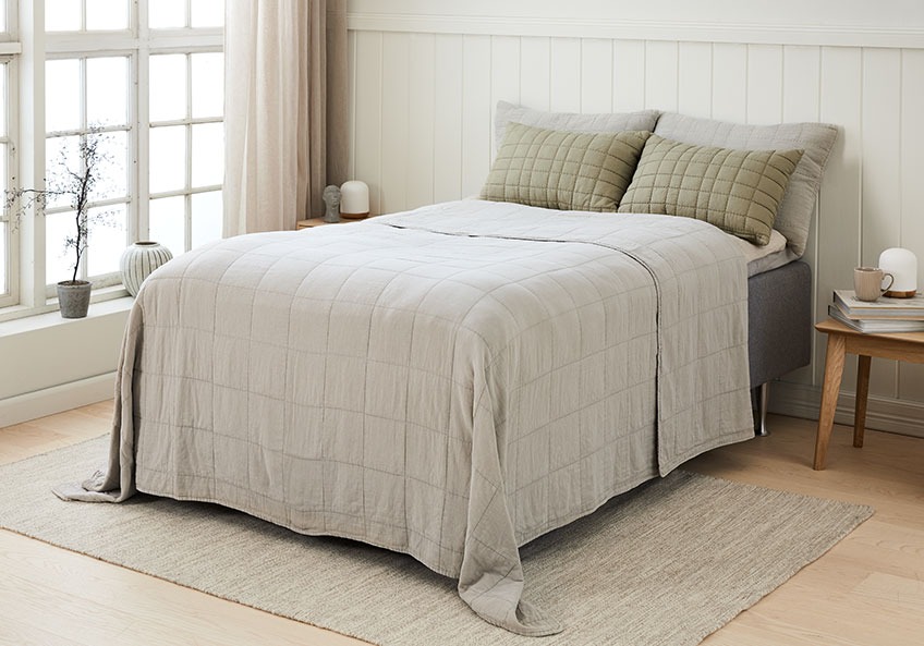 Κρεβάτι στρωμένο με κουβερλί και μαξιλάρια πλάτης σε ένα φωτεινό υπνοδωμάτιο