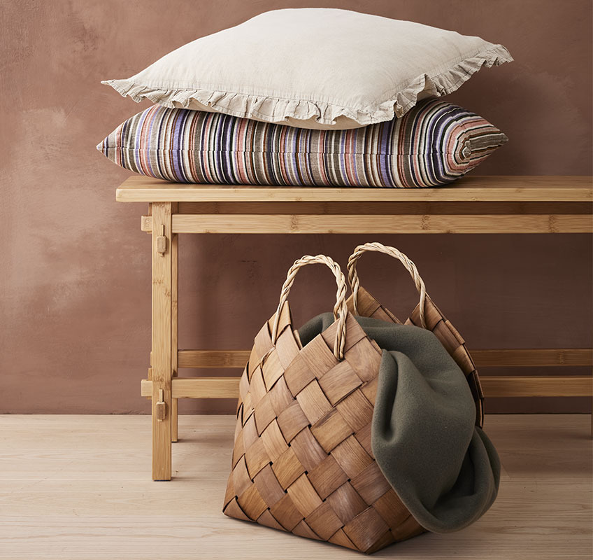 Διακοσμητικά μαξιλάρια πάνω σε ξύλινο πάγκο και καλάθι με ριχτάρι