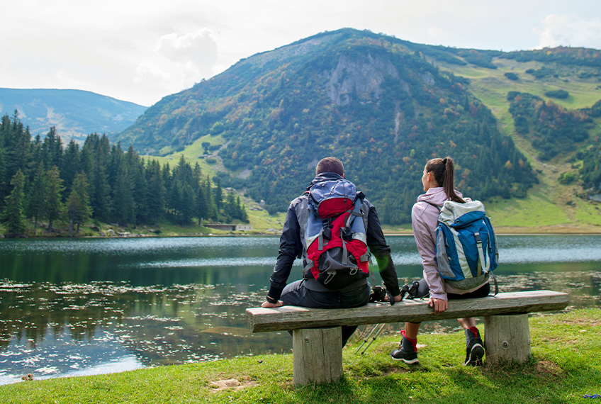 Άντρας και γυναίκα που κάθονται σε παγκάκι με θέα μια λίμνη και ένα βουνό